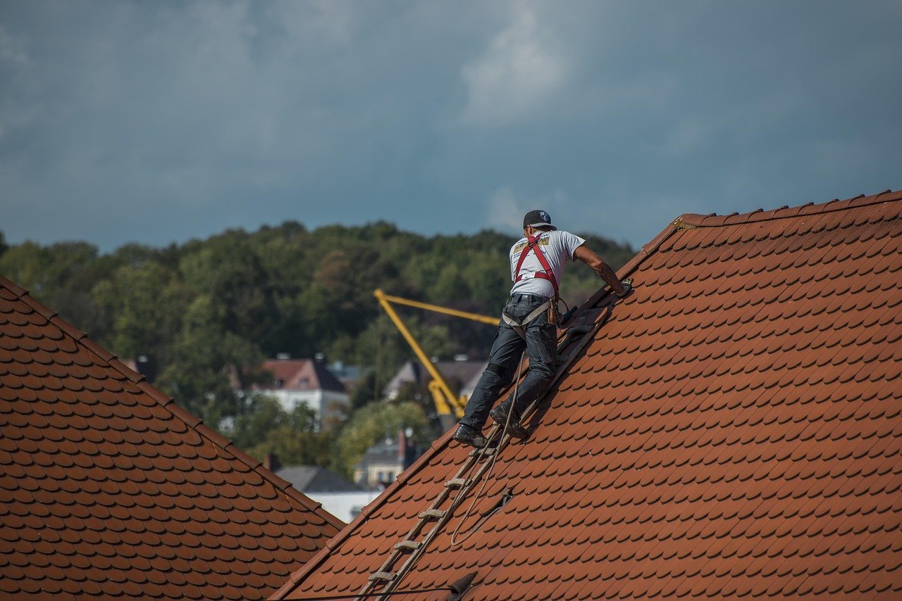 Roofing contractor in Royal Palm Beach working on a steep red-tiled roof with safety harness and ladder.