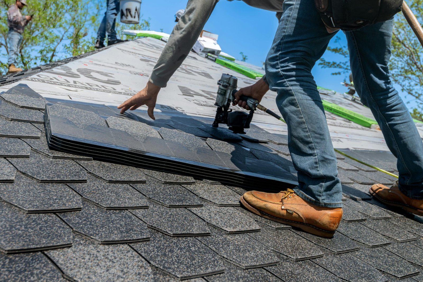 A roofing contractor in Royal Palm Beach placing asphalt shingles on a roof using a nail gun.
