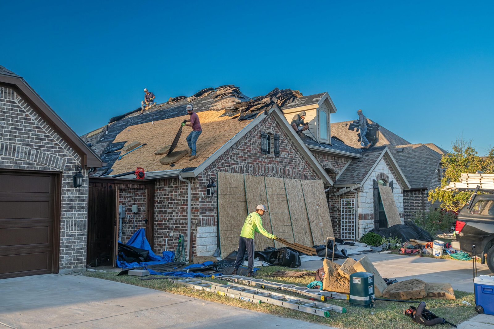 Team of roofing contractors in Royal Palm Beach replacing shingles on a large brick house.