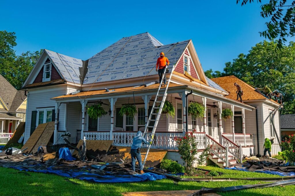 Roofing contractors in Royal Palm Beach replacing shingles on a residential home with protective tarps on the ground.